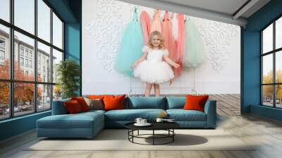 fancy dresses for girls. baby in a white, lush, elegant dress near the hanger with festive clothes. fashion for children. shop. Wall mural