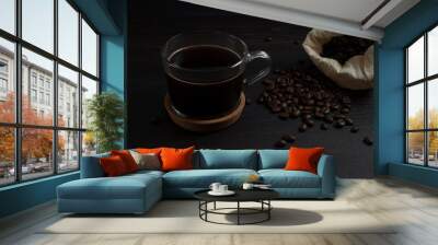 glass mug with fresh black natural coffee, a bag with coffee grains and sprinkled grains of roasted coffee on a wooden table Wall mural