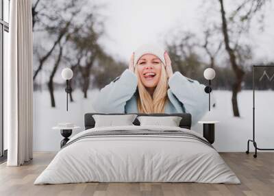 Cheerful blonde in the winter on the street stuck out her tongue and rejoices in the snow Wall mural