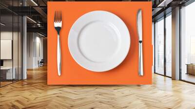 Knife, white plate and fork on orange background Wall mural