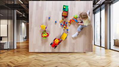 Little blond kid boy playing with colorful car toys on floor top view Wall mural