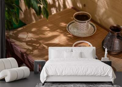 Two cups of coffee and cezve on the table in the patio lit by morning sun. Wall mural