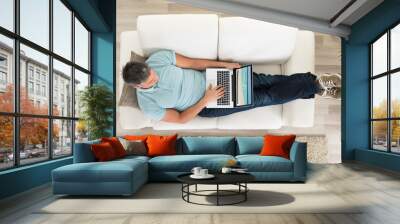 man sitting on sofa with laptop at home Wall mural