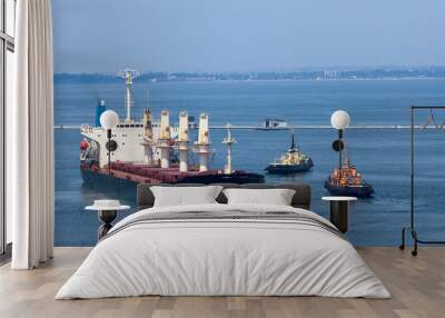 Cargo ship leaves port with tugs assistance Wall mural