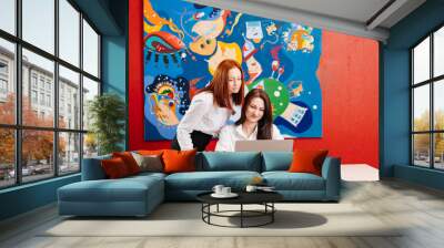 two women work together in an office on a laptop.  Wall mural