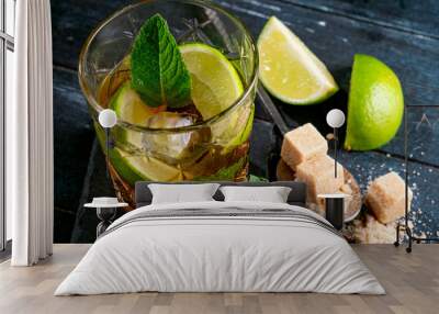 Whiskey and Cola cocktail with lime, mint, brown sugar and ice, alcoholic drink in a glass on a dark wooden background, copy space Wall mural