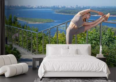 A young woman in a tracksuit performs physical exercises in a summer park Wall mural