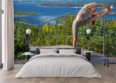 A young woman in a tracksuit performs physical exercises in a summer park Wall mural