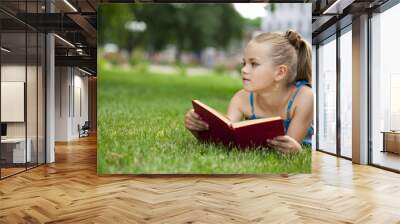 Adorable cute little girl reading book outside on grass Wall mural