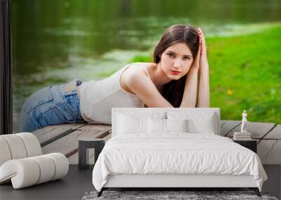 Young beautiful brunette girl in posing against the background of a pond in a summer park Wall mural