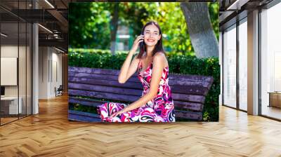 Young beautiful brunette woman calling by phone in summer park Wall mural