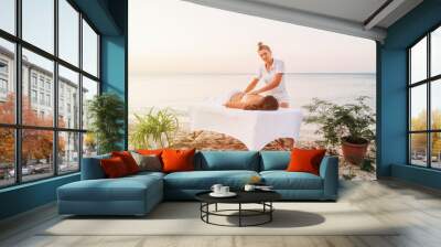 Girl masseur at work on background of seascape. Beach massage at resort. Portrait of masseur doing massage. Two girls at sea. Healthy lifestyle Wall mural