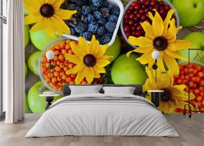 Berry and fruit background with autumn stocks still-life. Sea buckthorn, bird cherry, blackberries in jars with beautiful yellow flowers between twigs and ripe green apples. Top view, flat lay  Wall mural