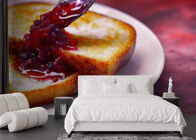 spoon drips sweet fresh natural raspberry jam and spreads over two pieces of toasted bread toast with Golden crust lying on white saucer on brown background Wall mural