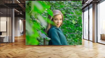 Portrait of a beautiful girl in a green coat on a background of ivy . Wall mural