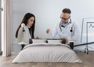 Male doctor fills out medical documentation during the female patient's appointment Wall mural