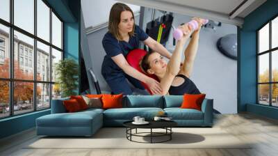 Physiotherapist helping sports woman to do exercises with dumbbells to recover from injury Wall mural