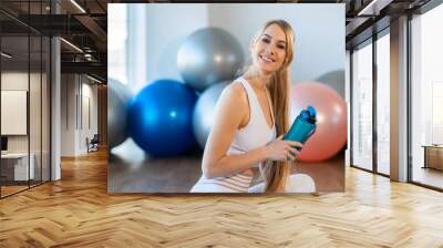 Portrait of beautiful fitness woman sitting on mat with sports bottle in her hands Wall mural