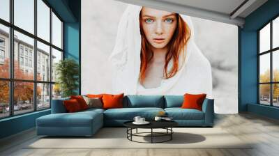 A beautiful young girl with red hair and freckles looks intently at the camera. Woman in the hood and clothes for the desert. Concept Wall mural