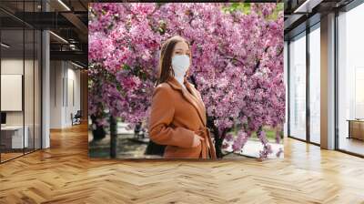 A young girl takes off her mask and breathes deeply after the end of the pandemic on a Sunny spring day, in front of blooming gardens. Protection and prevention covid 19 Wall mural