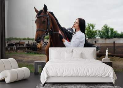 A young pretty girl rider poses near a thoroughbred stallion on a ranch. Horse riding, horse racing Wall mural