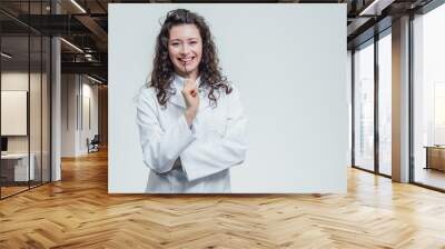 Beautiful smiling woman - the doctor looking at the camera half the turn. Happy and funny woman wearing a medical front portrait over a gray background. Medical Concepts. Wall mural