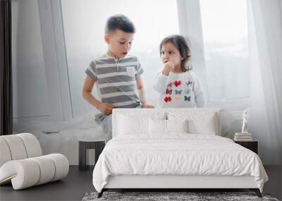 Brother and sister are sitting on the windowsill and reading a book. Happiness, family Wall mural