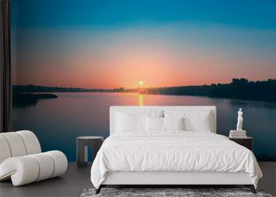 Pink Dawn: The sun rises over the blue calm water of the pond. A strip of sunlight is reflected in the blue surface of the water. Calm dawn landscape. Wall mural