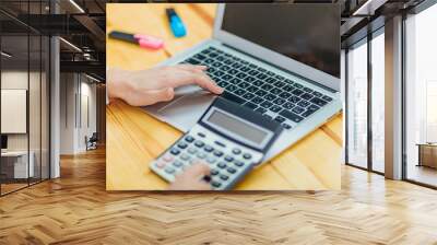 Close up of business woman holding hands with black calculator and laptop while sitting at desk in office background. Wall mural