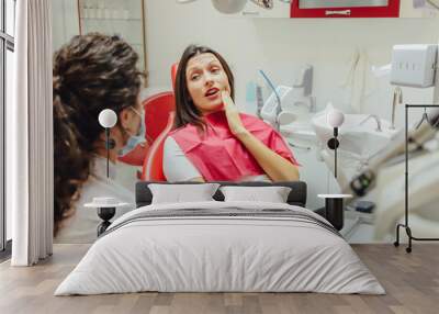 Close-up portrait of a sad young girl with a painful tooth, a doctor in office chairs, an isolated dentist office background clinic. E Wall mural