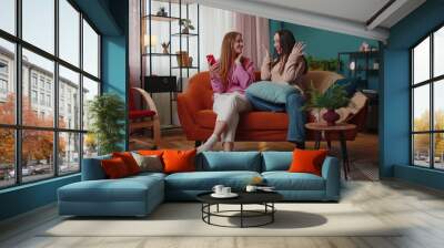 Cheerful girls friends siblings celebrate success win scream rejoices while doing online shopping on smartphone. Happy two female women couple family on sofa at home spend leisure time on mobile phone Wall mural