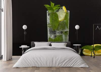 Clear water in glass with green mint leaves and ice cubes on black background Wall mural