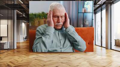 Displeased senior grandfather man rubbing temples to cure headache problem, suffering from tension and migraine, stress grimacing in pain high blood pressure at home. Elderly guy on couch. Lifestyles Wall mural