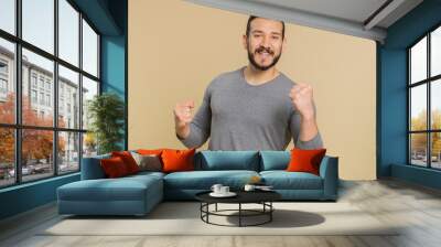 Happy joyful lebanese man shouting, raising fists in gesture I did it, celebrating success, winning, birthday, lottery jackpot goal achievemen, good news. Middle eastern guy on beige studio background Wall mural