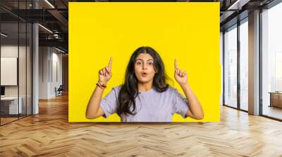 Indian woman showing thumbs up pointing overhead, above head empty place, advertising area for commercial text copy space for goods promotion advertisement. Arabian girl isolated on yellow background Wall mural