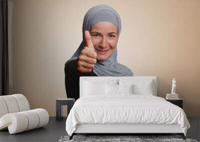 Like. Hipster muslim woman in hijab raises thumbs up agrees with something or gives positive reply recommends advertisement likes good. Young arabian girl isolated alone on beige studio background Wall mural