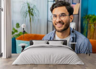 Portrait of happy calm Indian Arab man at home couch smiling friendly glad expression looking away dreaming resting relaxation feel satisfied good news celebrate win. Arabian young guy in living room Wall mural