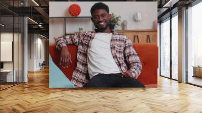 Portrait of happy one african american teenager student guy in casual shirt smiling, looking at camera. Young cute fashion model man indoors isolated at home in living room on sofa. Male nature beauty Wall mural