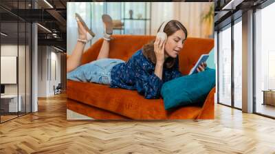 Portrait of happy overjoyed woman in wireless headphones relaxing lying on couch at home apartment choosing listening favorite energetic disco dancing music. People weekend daytime leisure activities. Wall mural