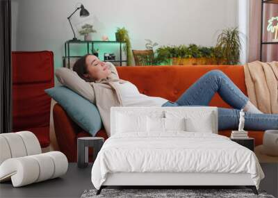 Portrait of tired young woman enjoy relaxing on home sofa in room. Happy pretty girl lying on couch resting napping after hard working day, closed her eyes, put hands behind head, stress free, rest Wall mural