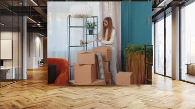 Woman entering room holding cardboard boxes, unpacking packages with interior stuff furniture after rental or buying new apartment home house. Girl concentrated on moving relocation. People lifestyle Wall mural