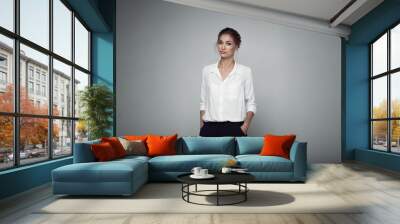 Interested businesswoman with trendy makeup posing on gray background in studio. Indoor photo of serious young lady in white blouses classic black pants standing in confident pose. Wall mural