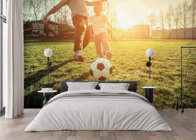 Father and son playing together with ball in football under sun Wall mural