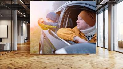 Happy father and son Sitting together in a new car on a journey. Family are resting on the side of the road on a road trip. Child takes pictures on smartphone. Happy family travels. Wall mural