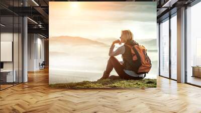 Happy woman tourist sitting on the green grass on the peak of mo Wall mural