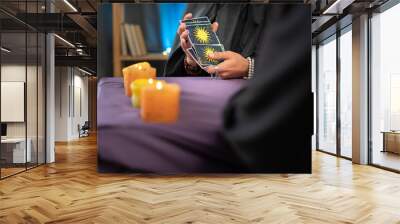 Close-up of a fortune tellers hand holding tarot cards over a table with candles, a future prediction session for a client Wall mural