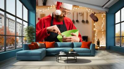 man in apron making dough for christmas gingerbread cookies mixing in green bowl while cooking in decorated kitchen Wall mural