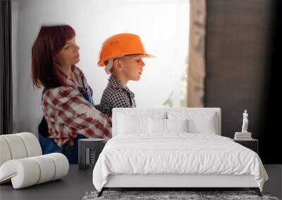 mom and son painting the wall together. repair apartments, a boy in an orange helmet and a woman whitewash the walls indoors. Home renovation concept Wall mural