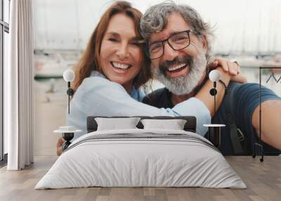 Close-up of smiling elderly couple taking selfie while standing in marina on yacht background Wall mural