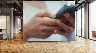 Closeup of young woman holds smartphone in her hands and scrolls through the news feed. Close-up of girl hand uses mobile phone outdoors Wall mural